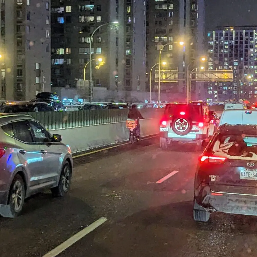 A cyclist riding a delivery ebike on the QEW highway among car traffic