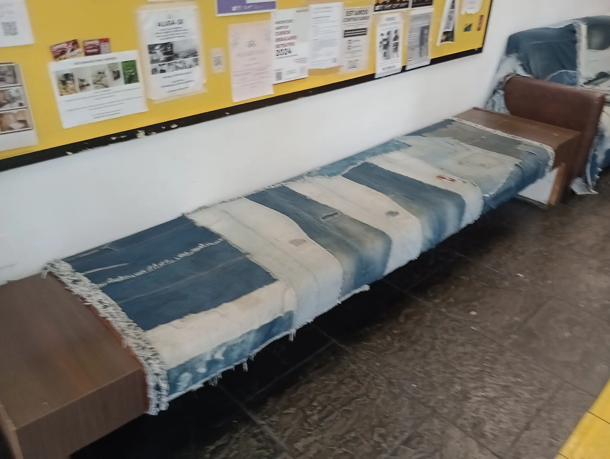 a wooden bench with a layer of jeans over most of it. a couch can be seen in the corner, also with a layer of jeans over most of it