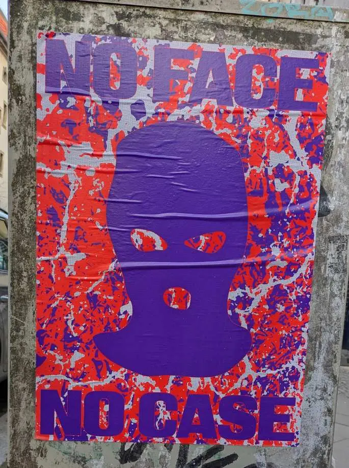 Violett Baclava with violett text "NO FACE - NO CASE" on orange and violett background as a poster pasted on a grey electrical box