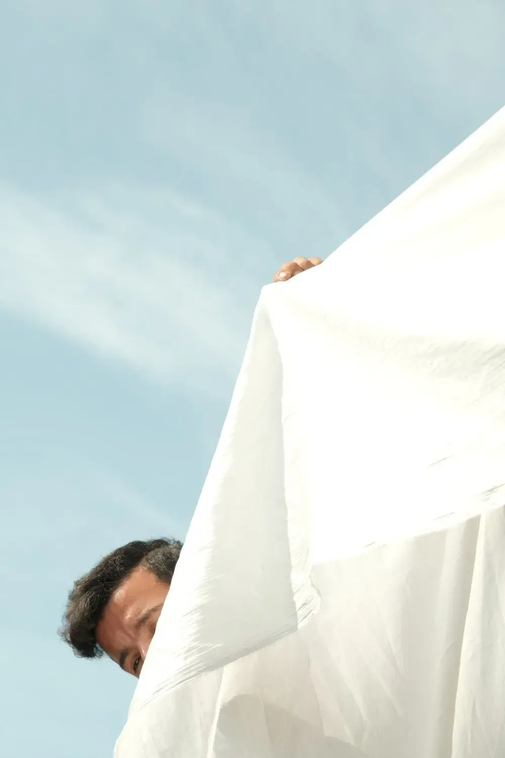 A man holding a white piece of fabric in front of himself, showing only a hand and the top of his head