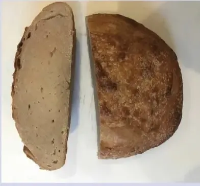 A baked round of bread without any air bubbles inside. The exterior is moderately burnt while the interior is a mass of semi-raw, burnt dough.