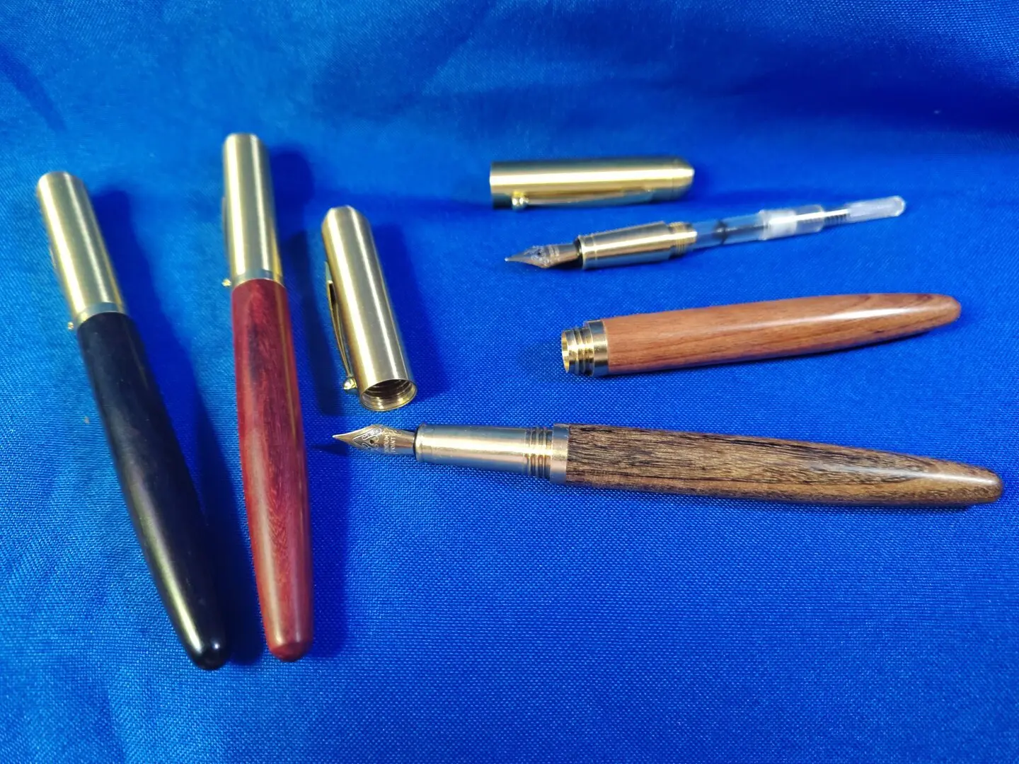 Four wood-barrelled fountain pens using four different woods, each with machined brass adapters, sections, and caps.